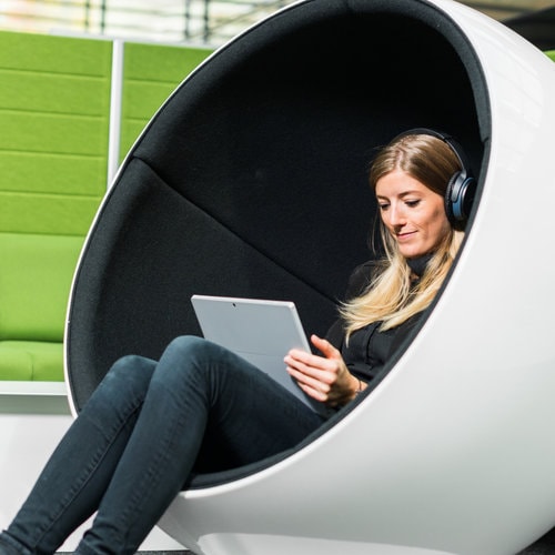A person is sitting in a white ball chair with a tablet and headphones on.