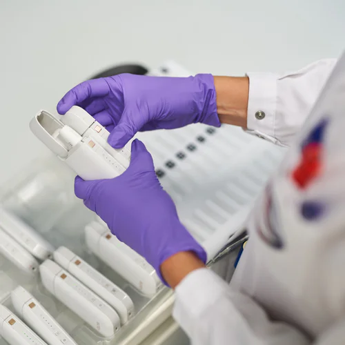 A scientist in a lab coat and rubber gloves holds heated tobacco product.