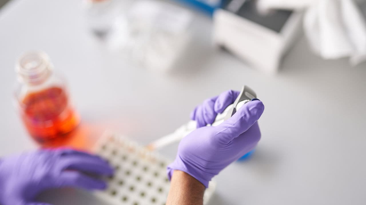 A scientist holds a pipette with rubber gloves.