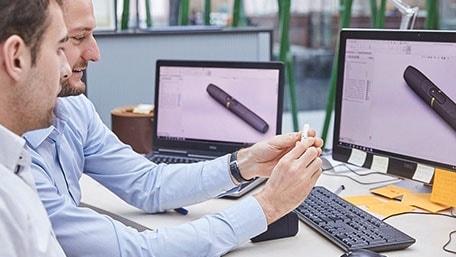 Close-up of two people in an office environment discussing over an smoke-free device.