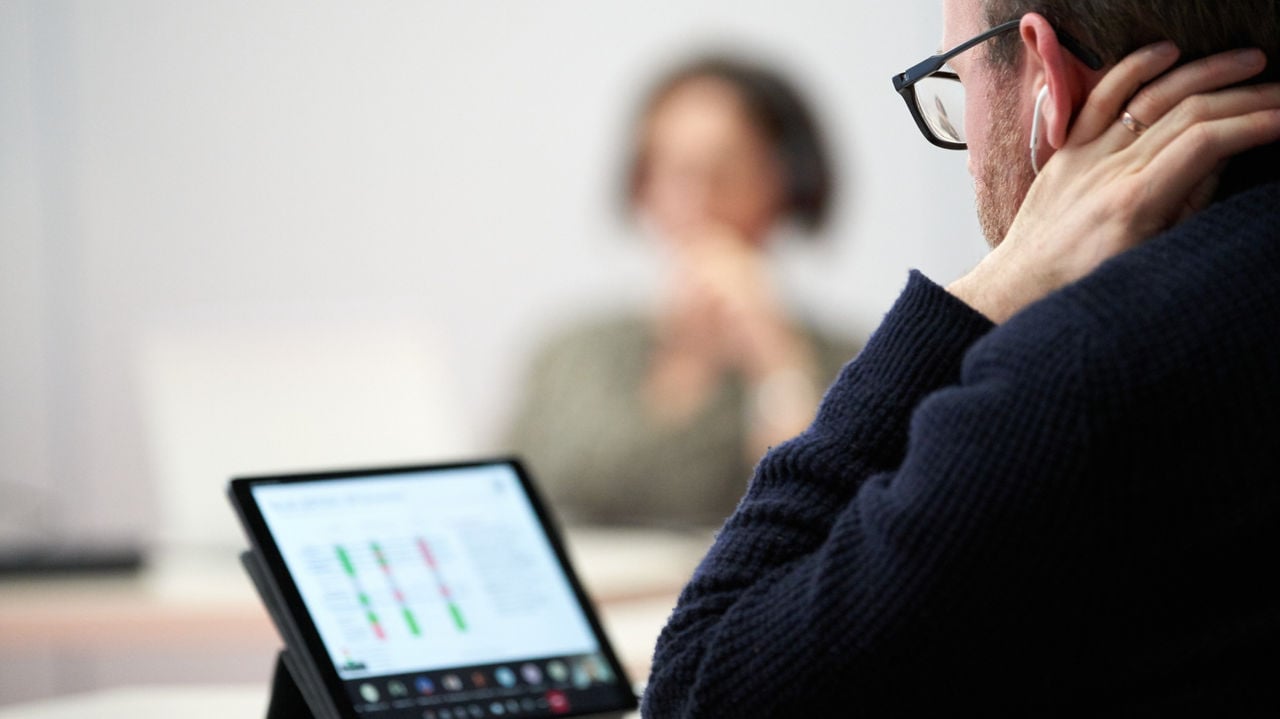 A man with glasses focused on data at tablet.