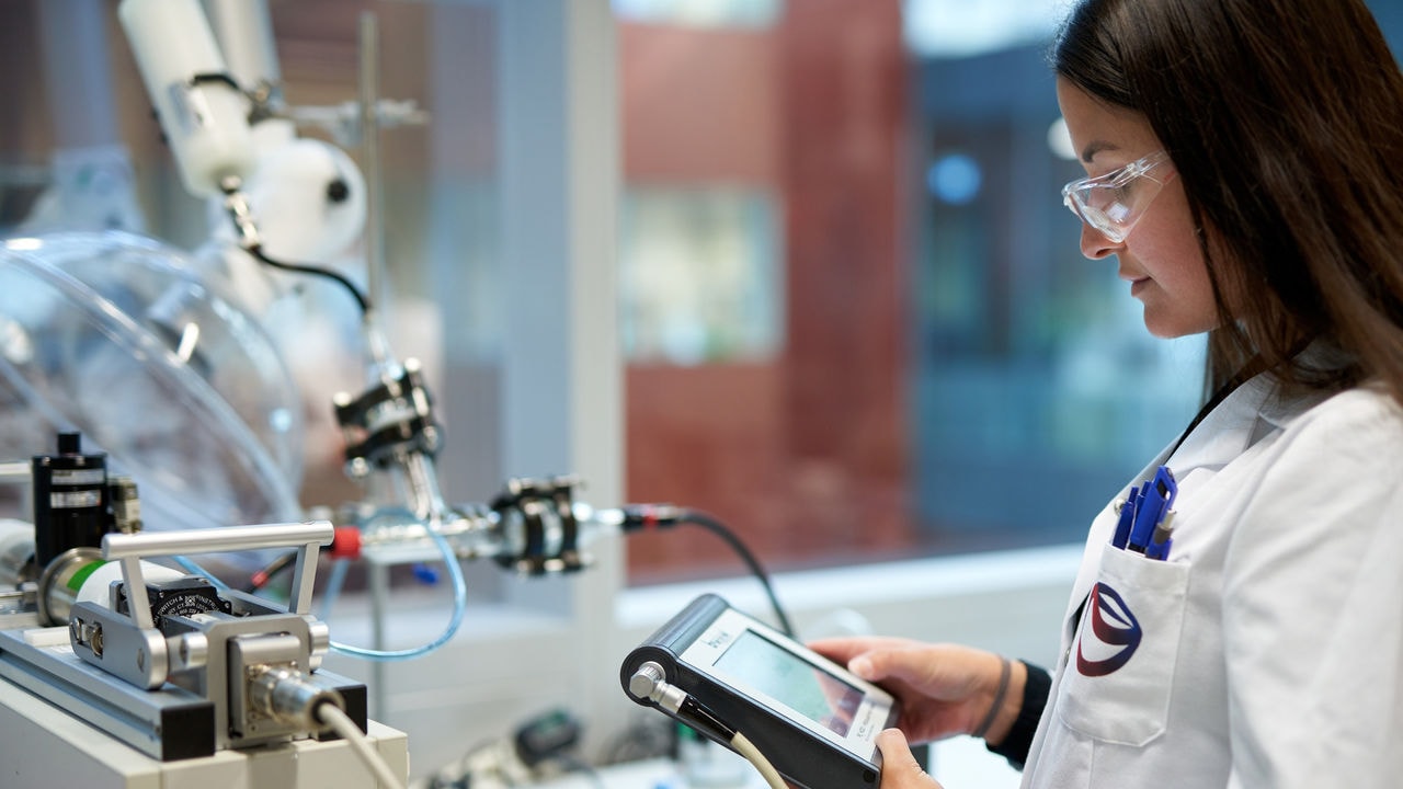 A scientist looks at a tablet device standing next to a machine in laboratory.