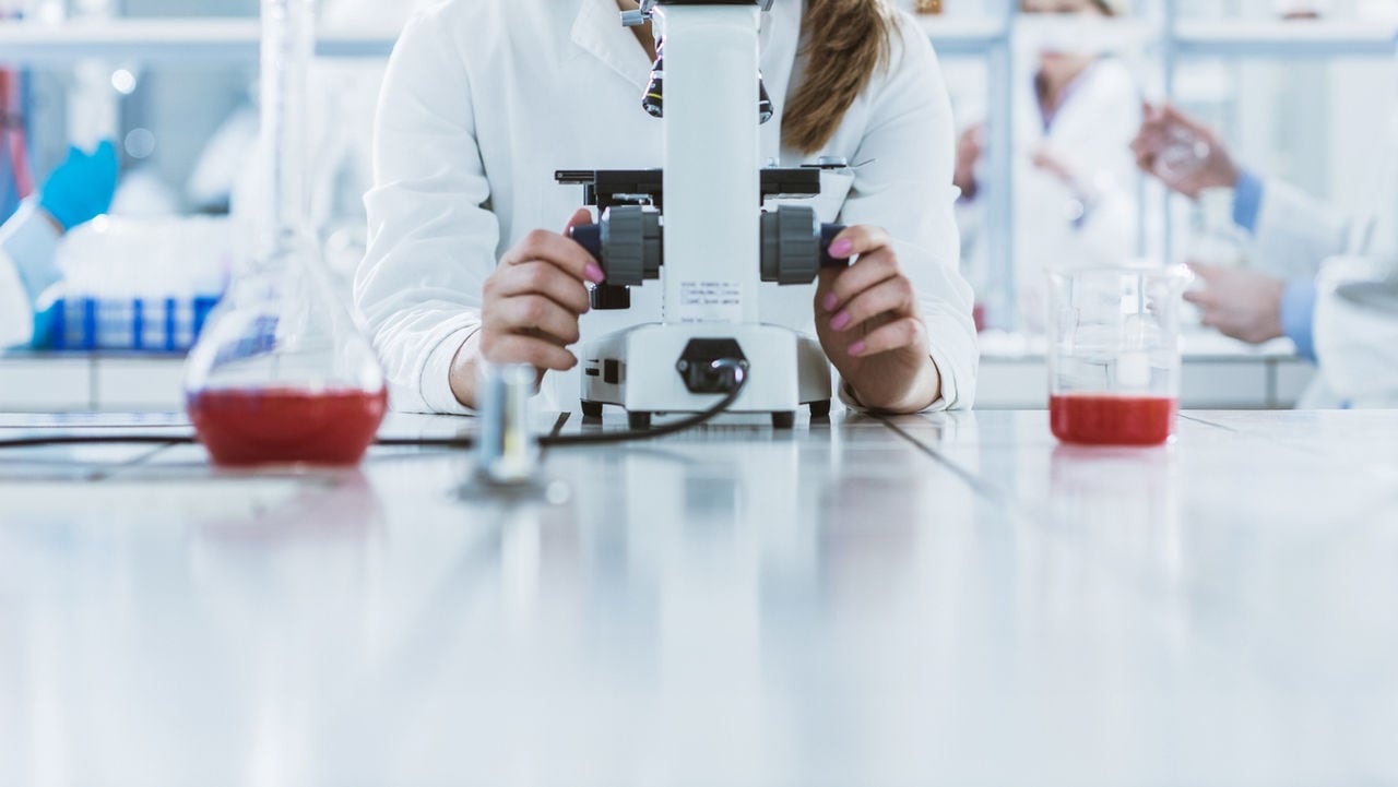 Young biochemist using microscope while working with her colleagues in a laboratory.
