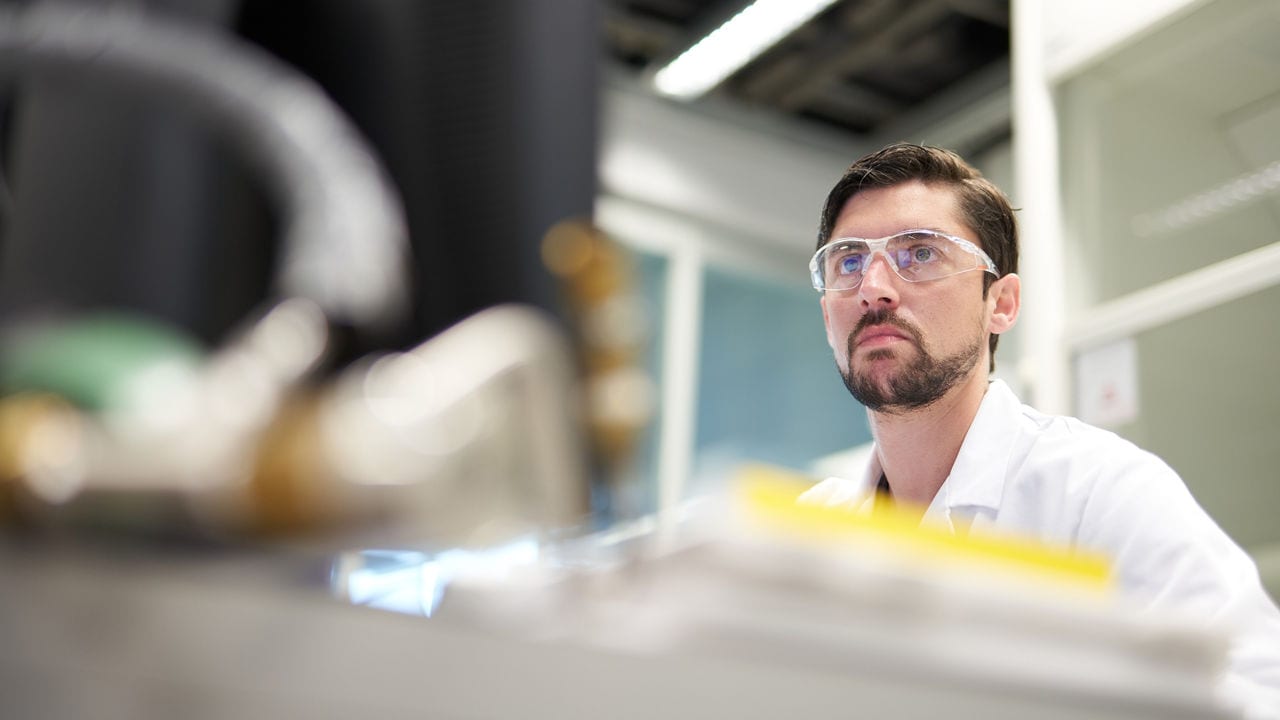 A scientist in a white lab coat with transparent glasses looking at computer.