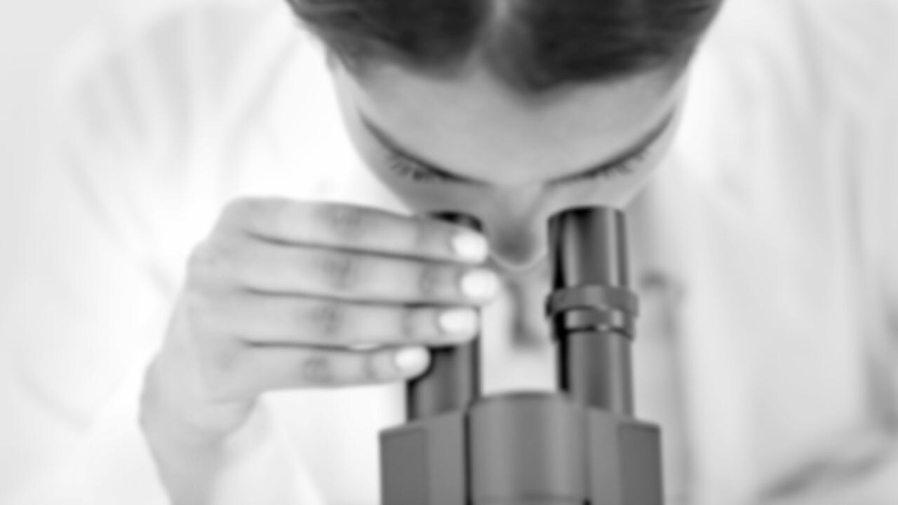 A scientist in a white coat looking through a microscope.