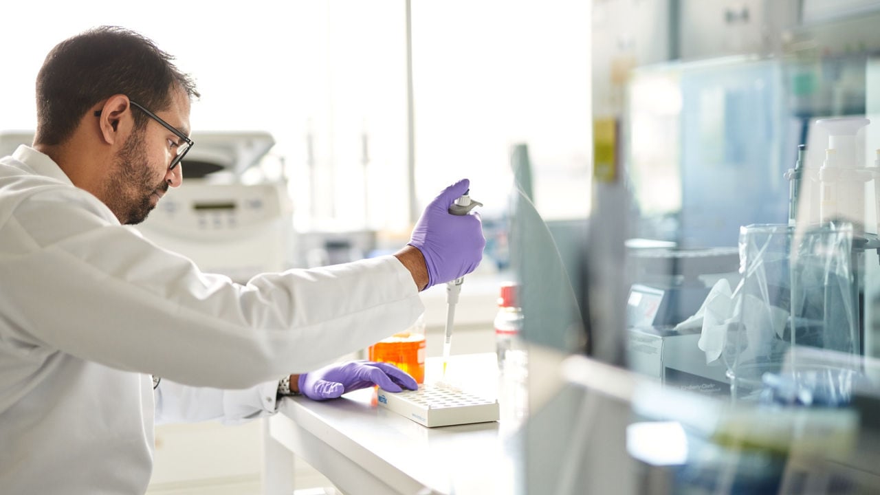 A scientist in white lab coat with rubber gloves conducting research.