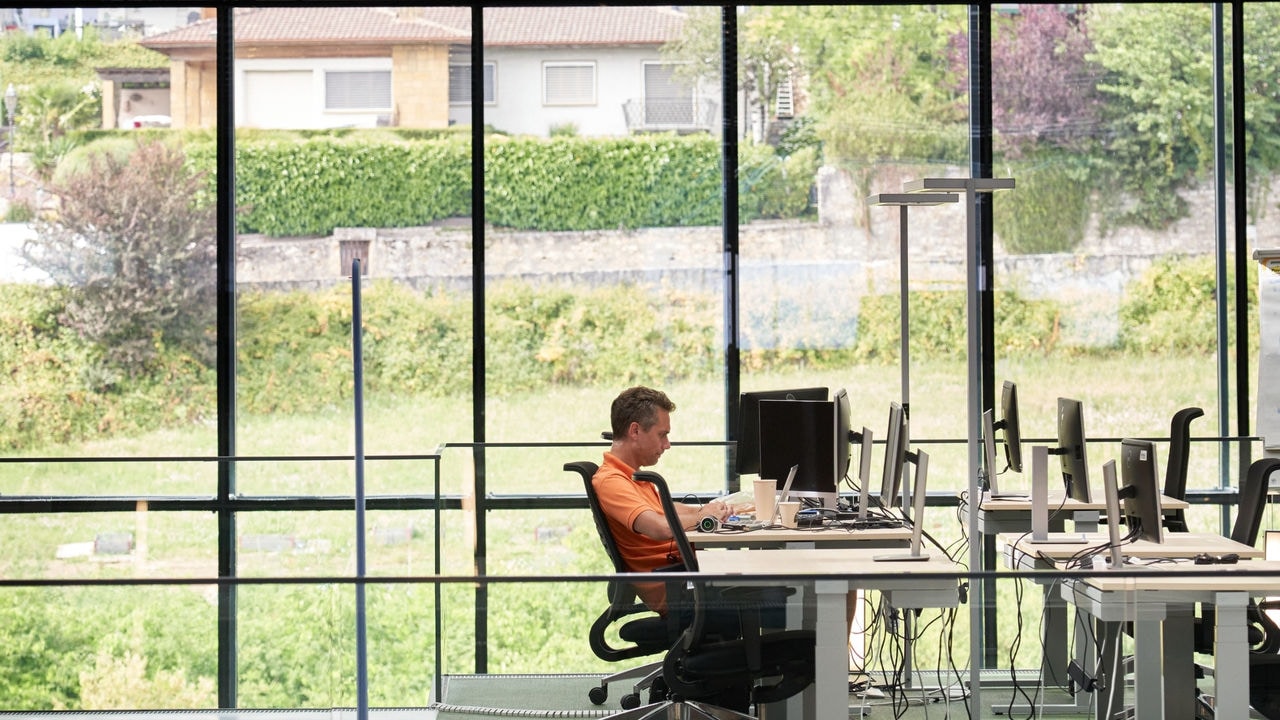 Employee sitting at a desk and working on a computer in a full-wall glass windows office.