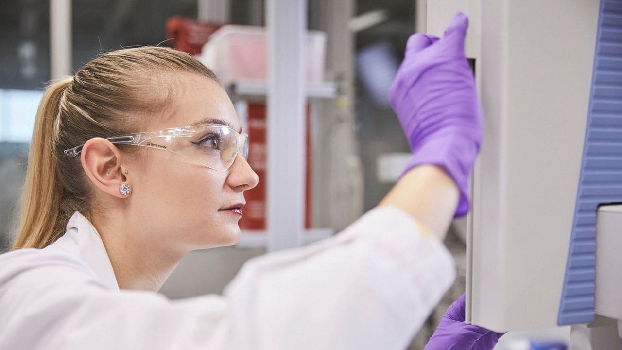 Scientist in laboratory wearing transparent glasses and purple gloves doing research.