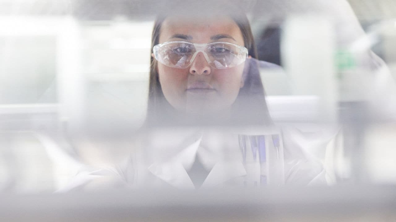 Blurred close-up of a scientist in laboratory wearing white lab coat and safety glasses.