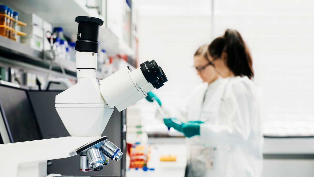 A close up of a laboratory microscope with scientists in the background.