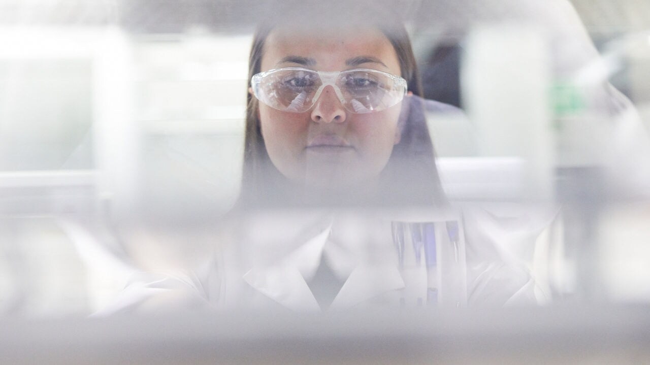 Blurred close-up of a scientist in laboratory wearing white lab coat and safety glasses.